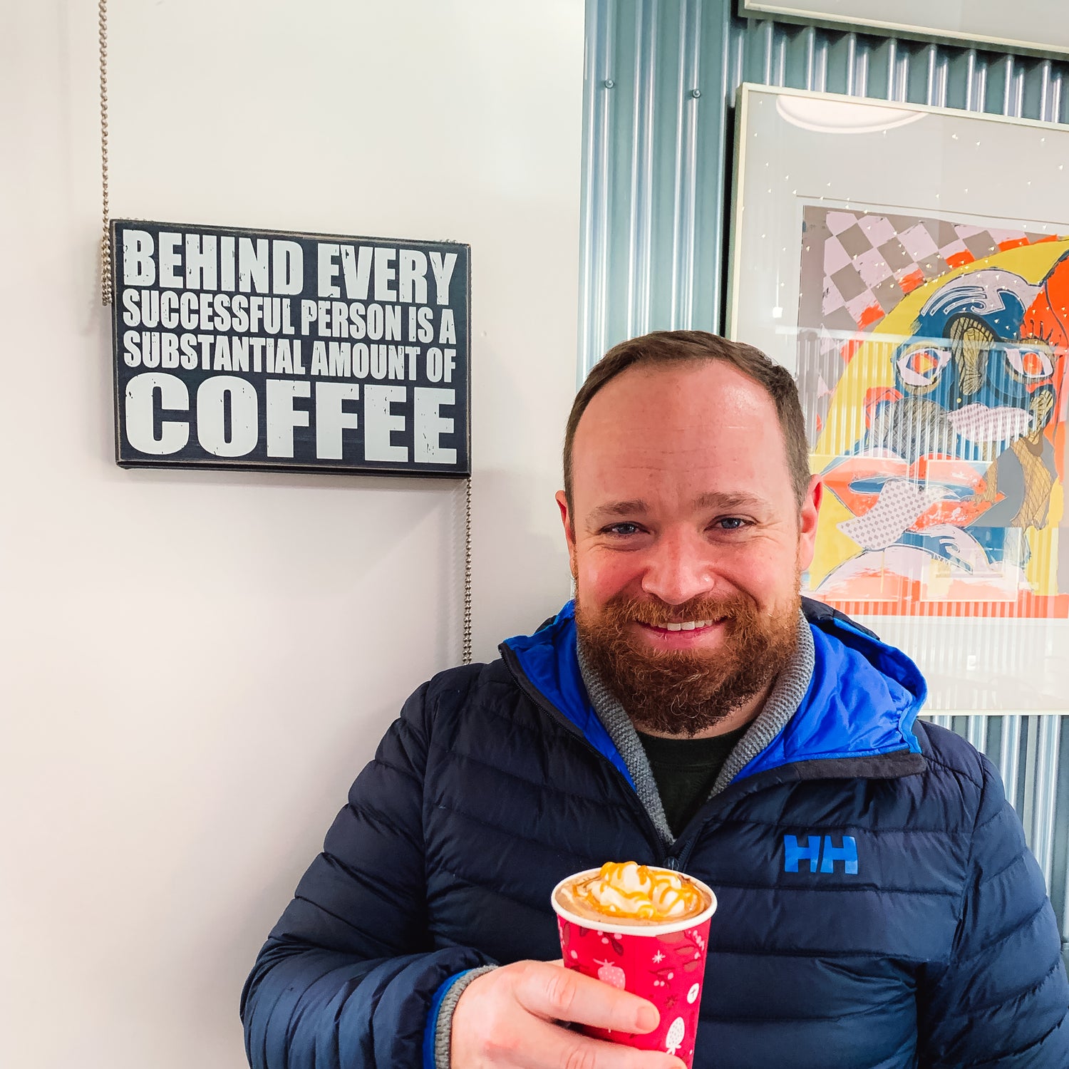 Man holding a coffee cup with a motivational sign about coffee behind him